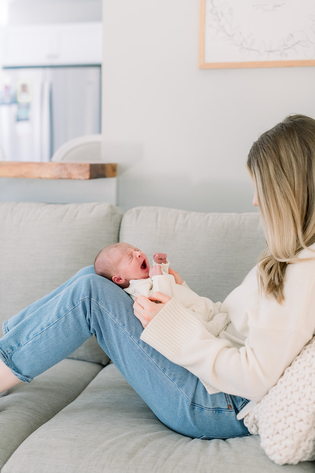 A newborn baby yawns thanks to mom and dad following newborn photo session tips while wearing a cream sweater on a couch