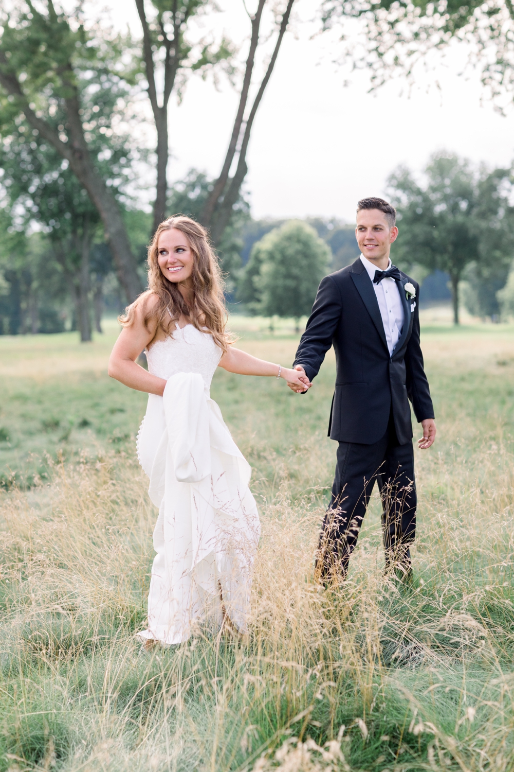 bride and groom holding hands in a field looking off camera while their westchester wedding photographer captures the moment
