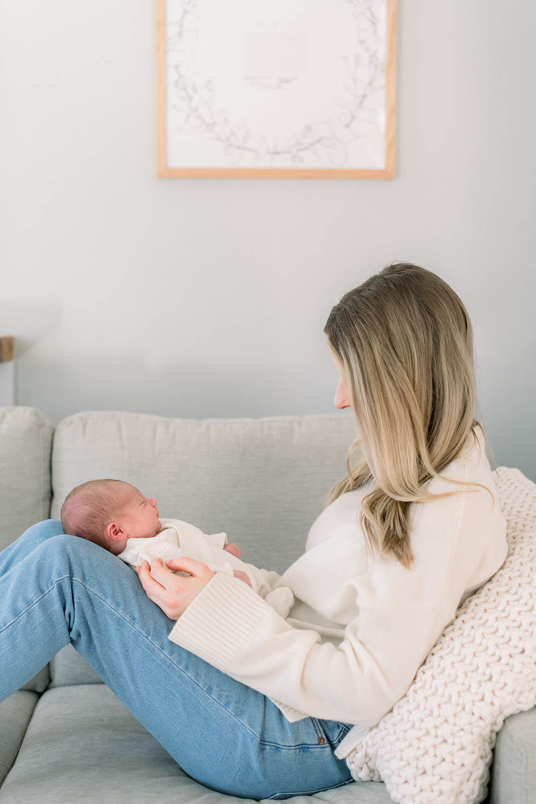 A profile look at a newborn baby sleeping in mom's lap with her knees up facing mom in a cream sweater after finding expert newborn photo session tips