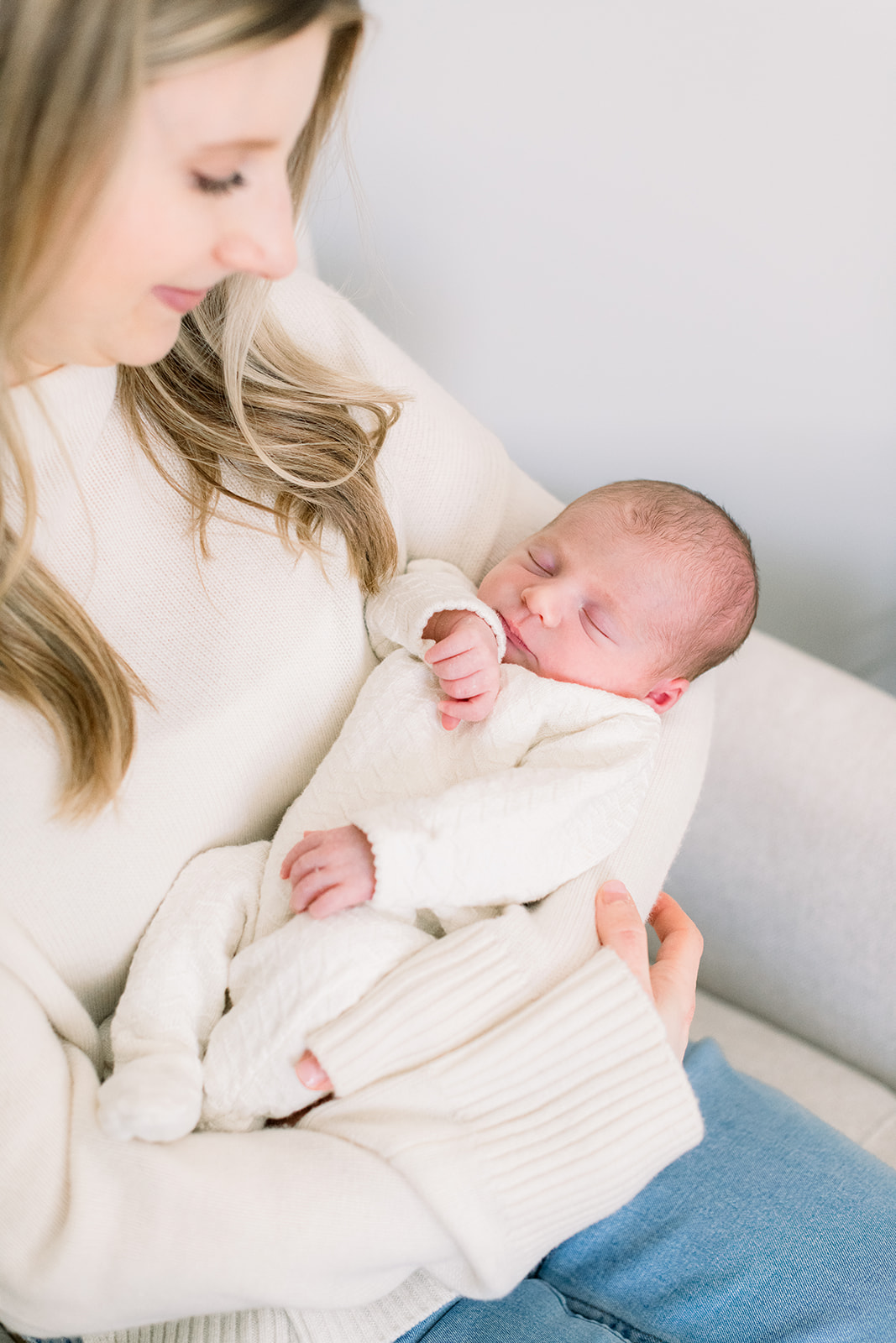 A look down at a newborn sleeping in mom's arms in a white onesie thanks to expert newborn photo session tips