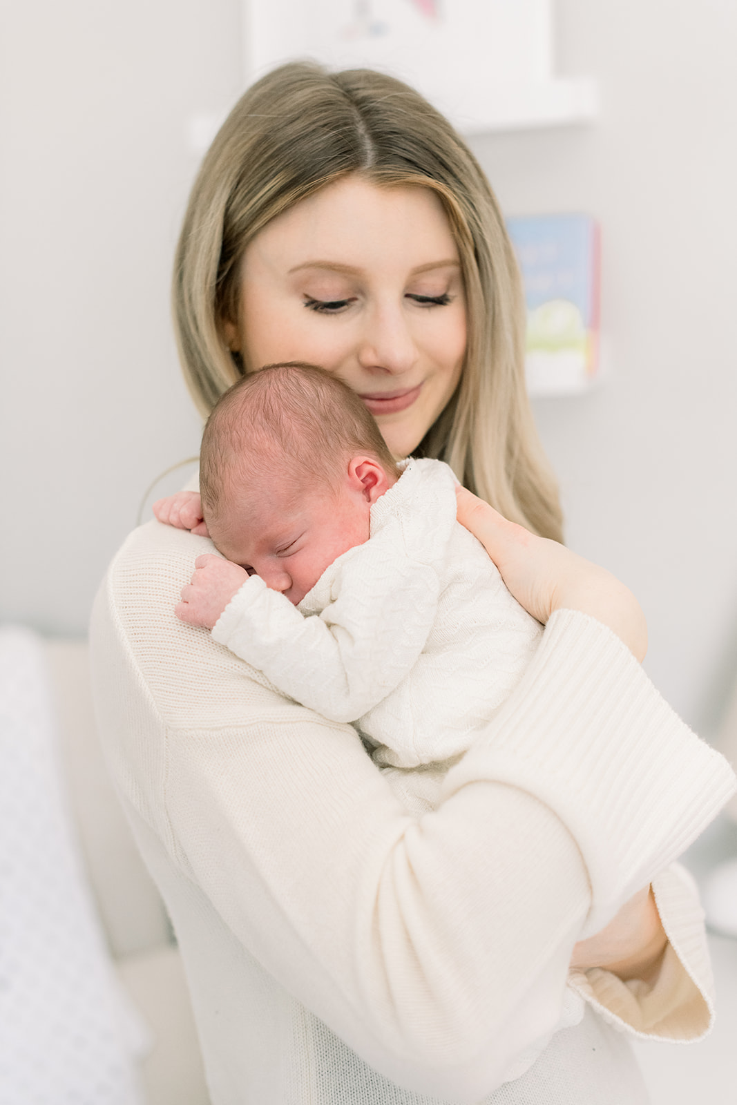 A happy mom snuggles her sleeping newborn on her shoulder while standing after learning these newborn photo session tips