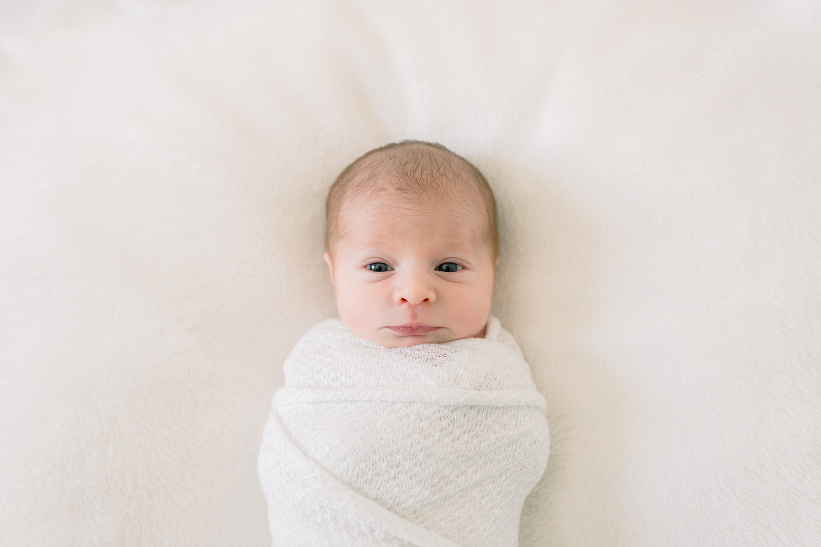 A closeup of an awake newborn abby laying swaddled in a bed thanks to expert newborn photo session tips