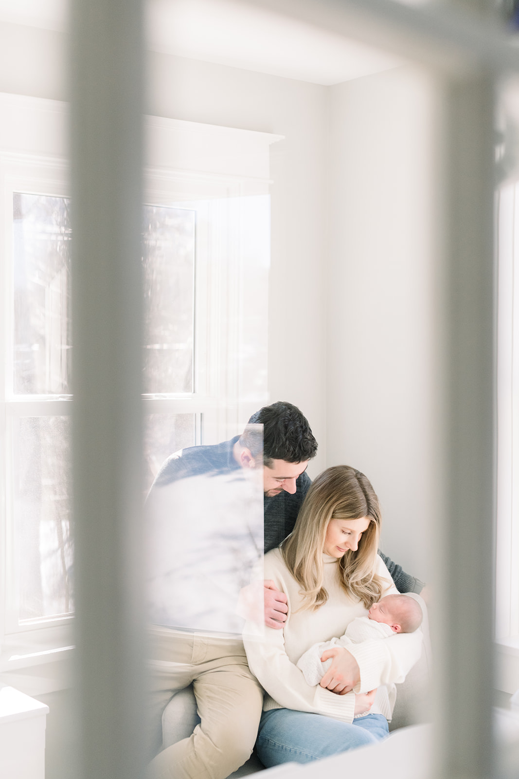 A peek at a mom and dad sitting on a nursing chair admiring their sleeping newborn baby